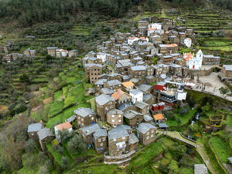 Aerial view of dark stone buildings nestled into the terraced landscape with a striking white church standing out against the muted tones Piódão Arganil Portugal. Aerial view of dark stone buildings nestled into the terraced landscape with a striking white church standing out against the muted tones Piódão Arganil Portugal.