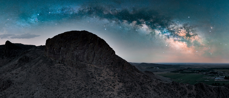 View of the Milky Way arching over a rugged mountain peak and a ranch in the valley below in Picabo Idaho United States.
