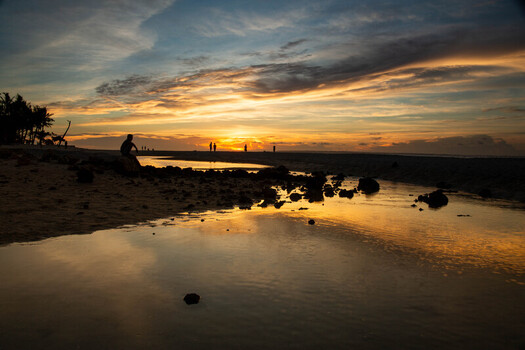 View of Bantayan Island beach at sunset with silhouettes of people calm water reflecting the orange sky and dark rocks on the sand in Cebu Central Visayas Philippines. View of Bantayan Island beach at sunset with silhouettes of people calm water reflecting the orange sky and dark rocks on the sand in Cebu Central Visayas Philippines.