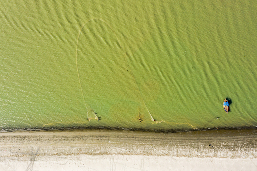 Aerial view of a small fishing boat and nets in the clear green water along the sandy beach of Kuakata Barisal Division Bangladesh. Aerial view of a small fishing boat and nets in the clear green water along the sandy beach of Kuakata Barisal Division Bangladesh.