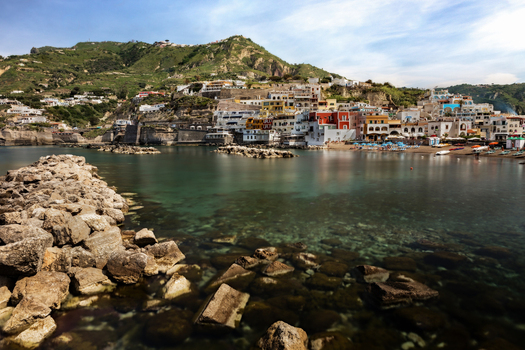 View of the coastal village of Sant Angelo featuring colorful houses and a rocky breakwater along the turquoise sea in Ischia Campania Italy. View of the coastal village of Sant Angelo featuring colorful houses and a rocky breakwater along the turquoise sea in Ischia Campania Italy.