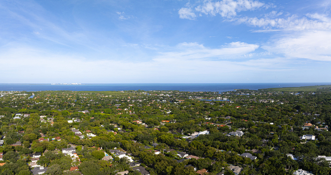 Aerial view of lush green residential neighborhoods with dense tree canopy and houses near the blue waters of Biscayne Bay under a clear sky Coral Gables Florida United States.