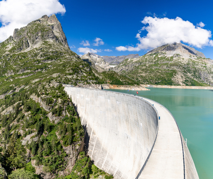 View of the massive concrete wall of the Emosson Dam holding back turquoise reservoir water surrounded by rugged alpine mountains and green slopes in Le Chatelard Fribourg Switzerland. View of the massive concrete wall of the Emosson Dam holding back turquoise reservoir water surrounded by rugged alpine mountains and green slopes in Le Chatelard Fribourg Switzerland.
