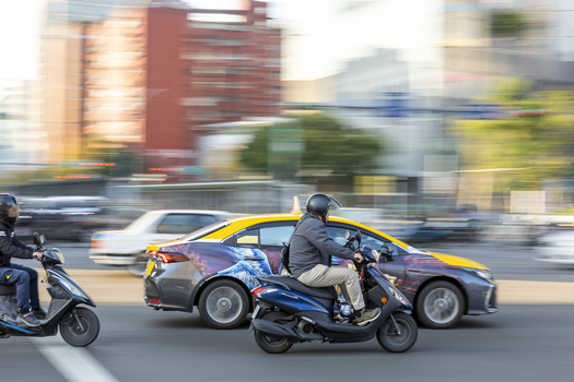 View of scooters with riders and cars rushing through a busy city intersection with motion blur and urban buildings in the background Taipei City Taiwan. View of scooters with riders and cars rushing through a busy city intersection with motion blur and urban buildings in the background Taipei City Taiwan.