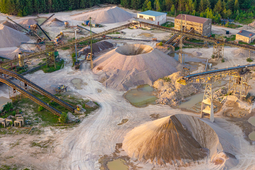 Aerial view of a large scale sand and gravel mine with industrial conveyor belts piles of extracted material and processing buildings surrounded by forest in Poland.