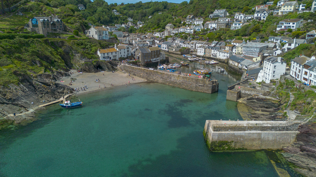 Aerial view of the coastal village of Polperro featuring a stone harbor wall turquoise waters fishing boats and historic cottages in Polperro Cornwall United Kingdom. Aerial view of the coastal village of Polperro featuring a stone harbor wall turquoise waters fishing boats and historic cottages in Polperro Cornwall United Kingdom.