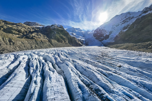 Aerial view of the vast icy expanse of the Morteratsch Glacier nestled between rugged snow dusted mountains under a brilliant sun kissed sky Morteratsch Glacier Grisons Switzerland. Aerial view of the vast icy expanse of the Morteratsch Glacier nestled between rugged snow dusted mountains under a brilliant sun kissed sky Morteratsch Glacier Grisons Switzerland.