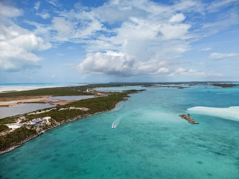 Aerial view of a boat cruising through turquoise waters near the Man O War Cay Sandbar and lush green coastline under a cloudy sky Rolletown Exuma The Bahamas. Aerial view of a boat cruising through turquoise waters near the Man O War Cay Sandbar and lush green coastline under a cloudy sky Rolletown Exuma The Bahamas.