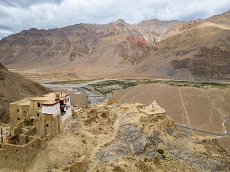 Aerial view of the ancient monastery and stupa perched on a rocky cliff overlooking the arid Zanskar valley with rugged mountains in the background Zanskar Ladakh India.