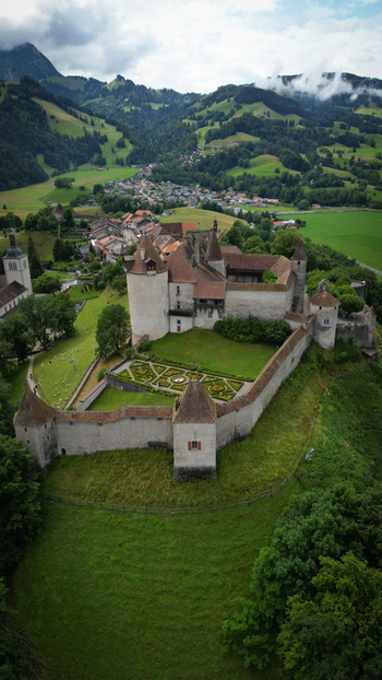 Aerial view of the medieval Gruy&egrave;res Castle its stone walls embracing history atop a verdant hill nestled amidst rolling green hills Gruy&egrave;res Fribourg Switzerland.