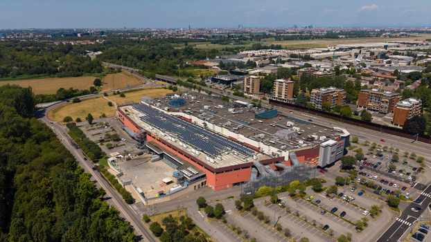 Aerial view of a large commercial building with solar panels on the roof surrounded by parking lots roads and greenery in Milan Lombardy Italy. Aerial view of a large commercial building with solar panels on the roof surrounded by parking lots roads and greenery in Milan Lombardy Italy.