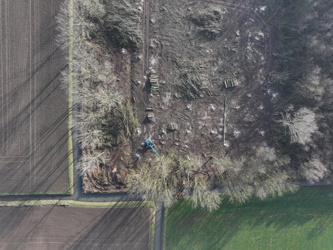 Aerial view of a deforested area with stacked logs a blue excavator working on the land and surrounding agricultural fields in the Netherlands. Aerial view of a deforested area with stacked logs a blue excavator working on the land and surrounding agricultural fields in the Netherlands.