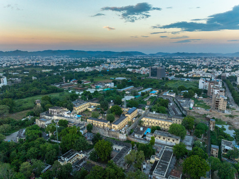 Aerial view of a historic palace complex surrounded by lush greenery and the urban landscape of Udaipur Rajasthan India.