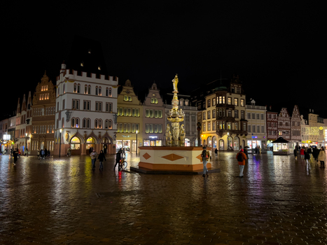 View of the historic Hauptmarkt square with the Petrusbrunnen fountain illuminated at night surrounded by traditional buildings and cobblestone streets in Trier Rheinland Pfalz Germany.