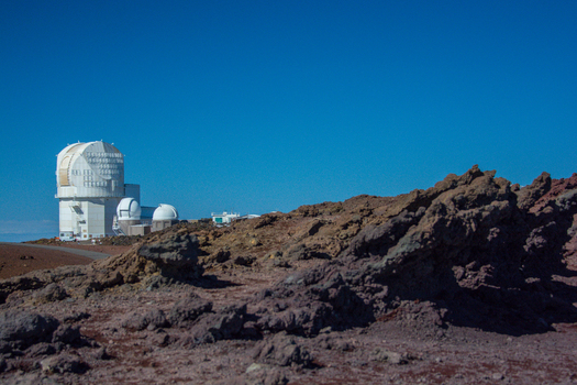 View of the Canada France Hawaii Telescope dome at the Mauna Kea Observatory surrounded by volcanic rocky terrain under a clear blue sky in Hawaii County Hawaii United States.