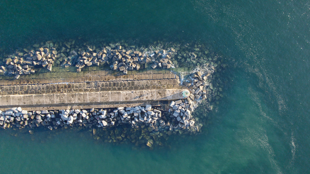 Aerial view of the stone breakwater pier in Ferragudo featuring large concrete blocks calm turquoise water and a small lighthouse at the end Ferragudo Faro District Portugal.