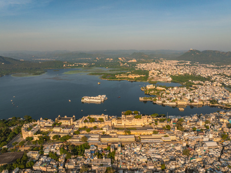 Aerial view of the historic City Palace complex situated on the banks of Lake Pichola with surrounding urban architecture and distant hills in Udaipur Rajasthan India.