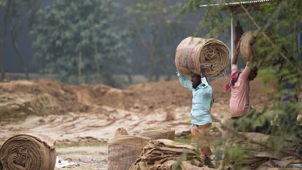 View of workers carrying large jute rolls on their heads Bangladesh.