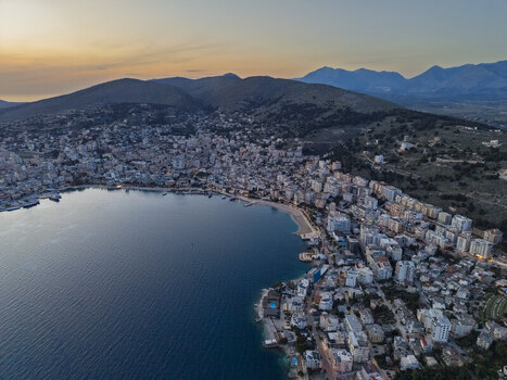Aerial view of the coastal city of Saranda nestled along the Ionian Sea with dense urban buildings hills in the background and a calm bay at sunset in Saranda Vlore County Albania. Aerial view of the coastal city of Saranda nestled along the Ionian Sea with dense urban buildings hills in the background and a calm bay at sunset in Saranda Vlore County Albania.