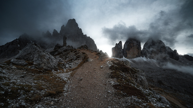 View of a rocky hiking trail leading towards the jagged peaks of the Dolomites under a dramatic cloudy sky in Trentino Alto Adige Italy. View of a rocky hiking trail leading towards the jagged peaks of the Dolomites under a dramatic cloudy sky in Trentino Alto Adige Italy.