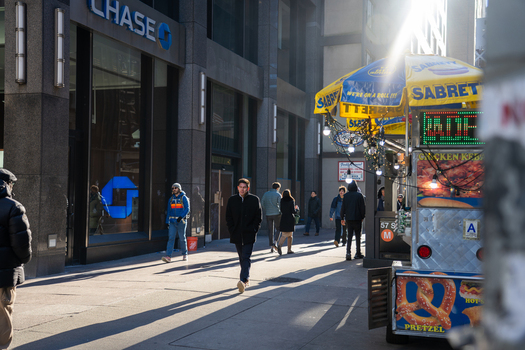 Manhattan United States 03 December 2025 View of pedestrians strolling along a sun drenched sidewalk near a Chase bank and a vibrant Sabrett hot dog cart capturing the essence of city life.
