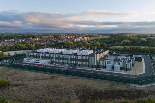 Aerial view of a modern data center facility with rooftop cooling units and a secure fenced perimeter in the United Kingdom. Aerial view of a modern data center facility with rooftop cooling units and a secure fenced perimeter in the United Kingdom.