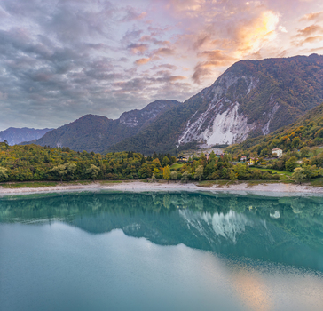 Aerial view of Lago di Tenno with its turquoise water reflecting the surrounding mountains and autumn forest under a soft sunset sky in Tenno Trentino Alto Adige Italy.
