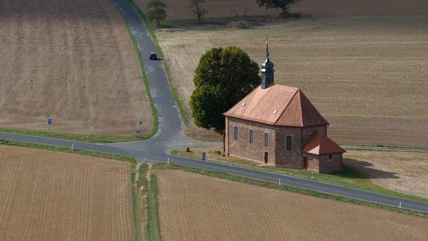 Aerial view of Wendelinuskapelle a historic stone chapel with a red tiled roof situated at a rural road intersection surrounded by agricultural fields in Dieburg Hessen Germany. Aerial view of Wendelinuskapelle a historic stone chapel with a red tiled roof situated at a rural road intersection surrounded by agricultural fields in Dieburg Hessen Germany.