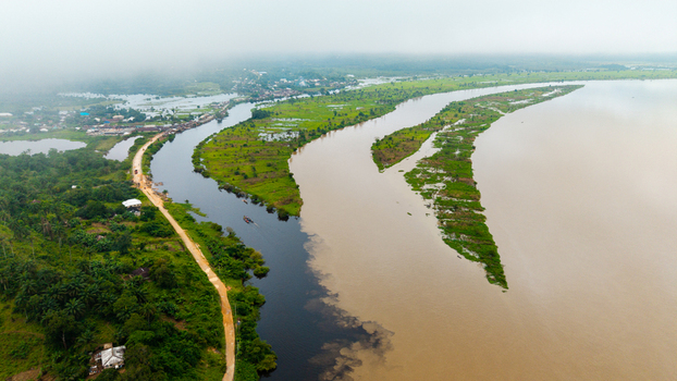 Aerial view of the Cross River and Calabar River confluence with lush green islands contrasting water currents and a dirt road winding through the landscape in Itu Akwa Ibom Nigeria. Aerial view of the Cross River and Calabar River confluence with lush green islands contrasting water currents and a dirt road winding through the landscape in Itu Akwa Ibom Nigeria.