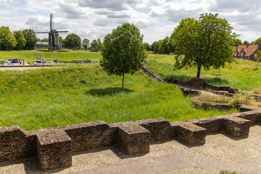 View of the historic brick fortification walls and a traditional windmill in the background surrounded by lush green grass and trees in Heusden North Brabant Netherlands.