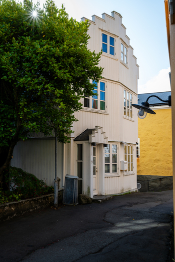 View of a traditional white wooden house with a stepped gable and large green tree in the Faroe Islands. View of a traditional white wooden house with a stepped gable and large green tree in the Faroe Islands.