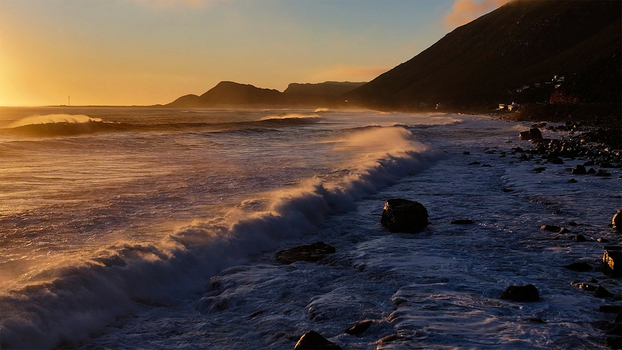 Aerial view of crashing waves along a rocky coastline with steep mountain slopes under a golden sunset sky Cape Town Western Cape South Africa. Aerial view of crashing waves along a rocky coastline with steep mountain slopes under a golden sunset sky Cape Town Western Cape South Africa.