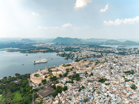 Aerial view of the historic City Palace complex situated on the banks of Lake Pichola with surrounding urban architecture and distant hills in Udaipur Rajasthan India. Aerial view of the historic City Palace complex situated on the banks of Lake Pichola with surrounding urban architecture and distant hills in Udaipur Rajasthan India.