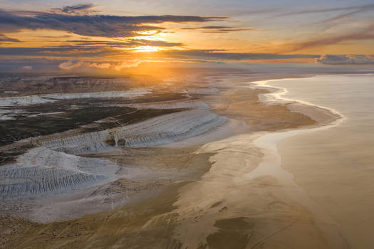 Aerial view of the Tuzbair salt flats at sunset featuring white limestone cliffs vast desert landscape and golden light in Mangystau District Mangystau Region Kazakhstan.