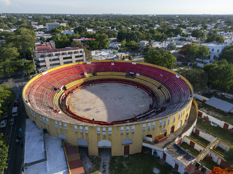 Aerial view of Plaza De Toros Merida a historic bullring with vibrant red and yellow seating surrounded by lush trees and urban buildings in Merida Yucatan Mexico. Aerial view of Plaza De Toros Merida a historic bullring with vibrant red and yellow seating surrounded by lush trees and urban buildings in Merida Yucatan Mexico.