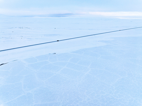 Aerial view of a vast snow covered landscape with a single road stretching across the frozen patterned terrain in Egilsstadir Mulathing Iceland. Aerial view of a vast snow covered landscape with a single road stretching across the frozen patterned terrain in Egilsstadir Mulathing Iceland.