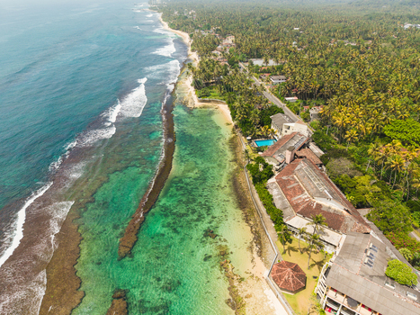 Aerial view of Thalpe Beach featuring turquoise waters coral reefs and lush palm trees along the coastline in Talpe Southern Province Sri Lanka. Aerial view of Thalpe Beach featuring turquoise waters coral reefs and lush palm trees along the coastline in Talpe Southern Province Sri Lanka.