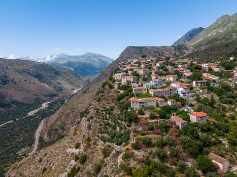 Aerial view of stone houses of an old village on a steep mountain slope with lush green vegetation and a winding road in the valley below Qeparo Fshat Vlore County Albania. Aerial view of stone houses of an old village on a steep mountain slope with lush green vegetation and a winding road in the valley below Qeparo Fshat Vlore County Albania.