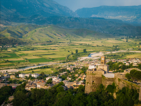 Aerial view of the historic Gjirokaster Castle with its clock tower overlooking the old town and the green Drino river valley Gjirokaster Gjirokaster County Albania. Aerial view of the historic Gjirokaster Castle with its clock tower overlooking the old town and the green Drino river valley Gjirokaster Gjirokaster County Albania.