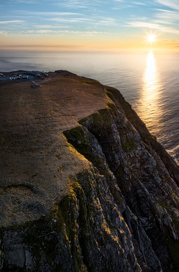 Aerial view of the dramatic cliffs of North Cape bathed in golden hour light with the vast ocean stretching to the horizon in Nordkapp Municipality Finnmark Norway. Aerial view of the dramatic cliffs of North Cape bathed in golden hour light with the vast ocean stretching to the horizon in Nordkapp Municipality Finnmark Norway.