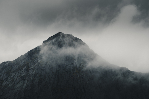 View of the dramatic rocky peak of Lofoten mountain partially shrouded in thick low hanging clouds under a moody overcast sky in Nordland Norway.