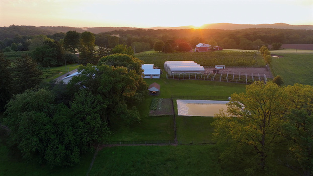 Aerial view of Flintrock farm at sunset featuring greenhouses a small pond lush green fields and rolling hills in Elizabeth Township Pennsylvania United States.