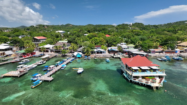 Aerial view of West End with its waterfront wooden piers colorful boats and a restaurant over the turquoise sea surrounded by lush hills in West End Bay Islands Department Honduras. Aerial view of West End with its waterfront wooden piers colorful boats and a restaurant over the turquoise sea surrounded by lush hills in West End Bay Islands Department Honduras.