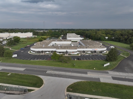 Aerial view of a modern commercial office building with a central courtyard and surrounding parking lot situated near green spaces and a road in Indianapolis Indiana United States. Aerial view of a modern commercial office building with a central courtyard and surrounding parking lot situated near green spaces and a road in Indianapolis Indiana United States.