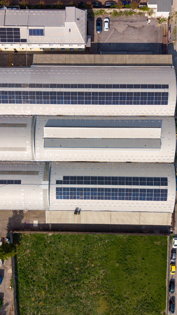Aerial view of an industrial building featuring large arched roofs equipped with extensive solar panel arrays situated next to a grassy lot and parking area in Milan Lombardy Italy.