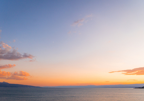 View of the sunset over Lake Geneva with distant mountains and a crescent moon in the sky in Bourg en Lavaux Vaud Switzerland. View of the sunset over Lake Geneva with distant mountains and a crescent moon in the sky in Bourg en Lavaux Vaud Switzerland.