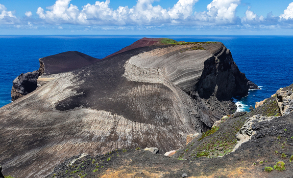 Aerial view of the volcanic landscape of Capelinhos where black earth meets the azure sea creating a stark contrast under a bright sky Capelo A&ccedil;ores Portugal.