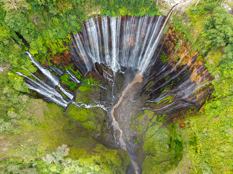 Aerial view of Tumpak Sewu Waterfall cascading down a lush steep canyon wall surrounded by dense tropical rainforest and vibrant green vegetation in Kecamatan Pronojiwo Jawa Timur Indonesia. Aerial view of Tumpak Sewu Waterfall cascading down a lush steep canyon wall surrounded by dense tropical rainforest and vibrant green vegetation in Kecamatan Pronojiwo Jawa Timur Indonesia.