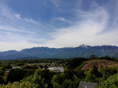 Aerial view of the Yatsugatake Mountains rising above lush green foothills and rural fields under a blue sky with wispy clouds in Chino Nagano Japan. Aerial view of the Yatsugatake Mountains rising above lush green foothills and rural fields under a blue sky with wispy clouds in Chino Nagano Japan.