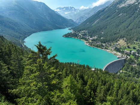 Aerial view of Lago di Ceresole featuring the turquoise alpine lake a concrete dam and lush pine forests under rugged mountain peaks in Ceresole Reale Piedmont Italy. Aerial view of Lago di Ceresole featuring the turquoise alpine lake a concrete dam and lush pine forests under rugged mountain peaks in Ceresole Reale Piedmont Italy.